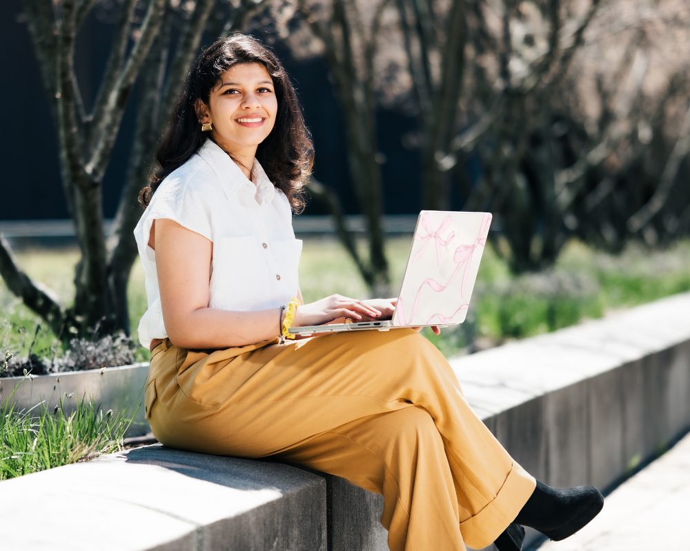UConn MBA student sitting on a park bench with a laptop on a sunny day