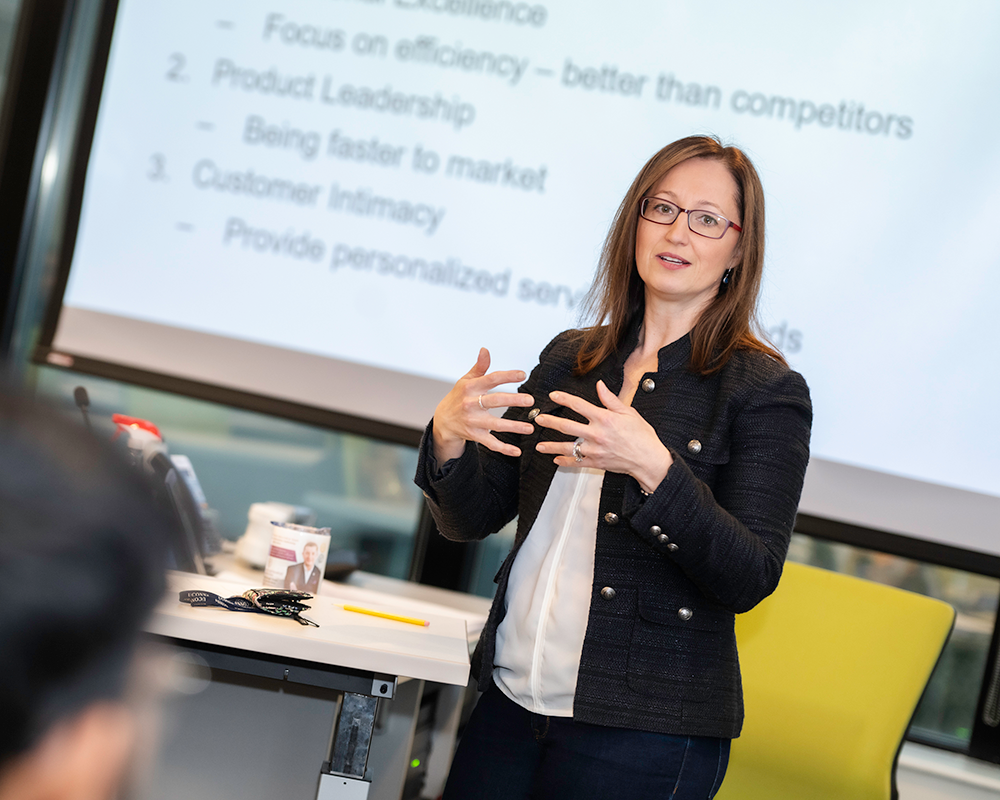 A UConn School of Business course instructor standing in front of a class of students explaining business concepts