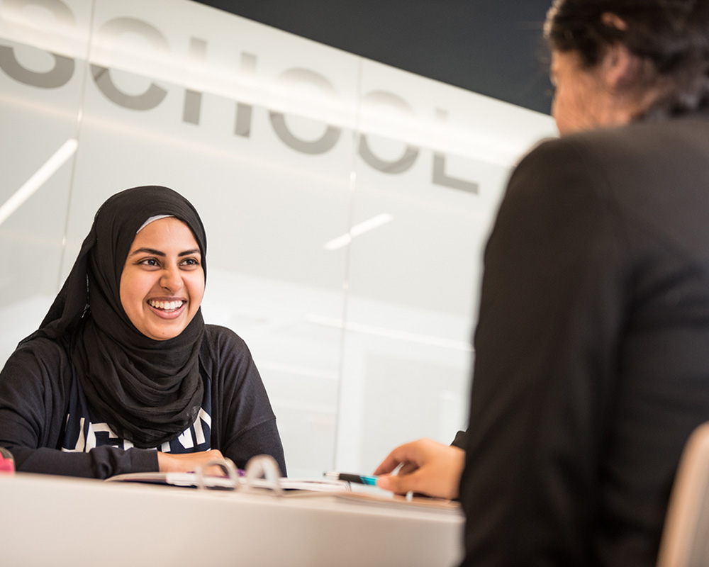 Smiling student seated at a table talking to career advisor at the School of Business
