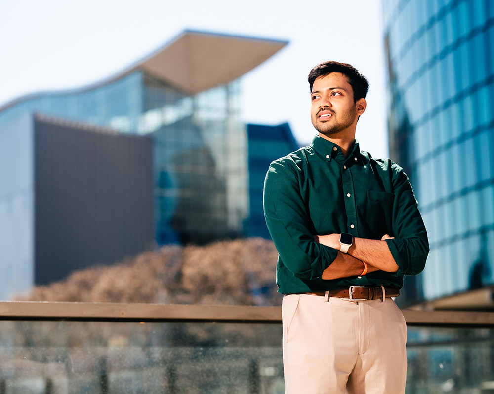 A business student with arms crossed looking into the distance standing outdoors in front of Hartford Connecticut office buildings